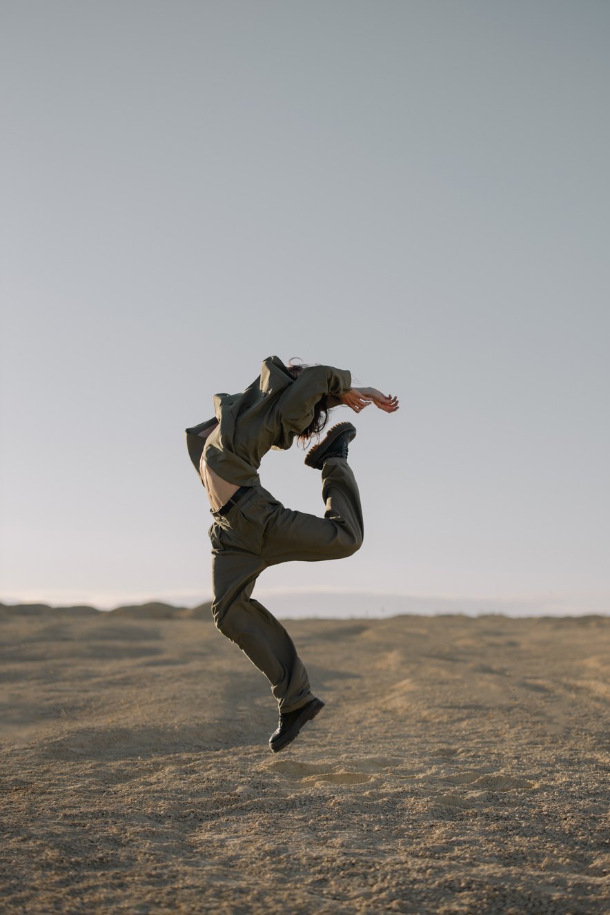 Man in Brown Jacket and Brown Pants Jumping on Brown Field